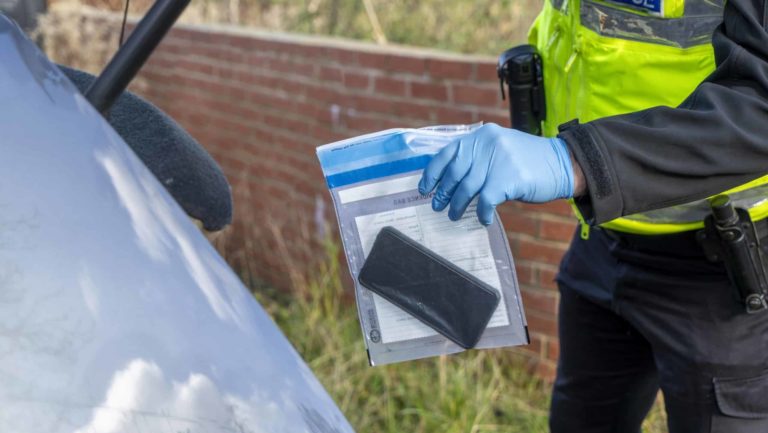 UK police officer with an evidence bag and confiscated mobile phone
